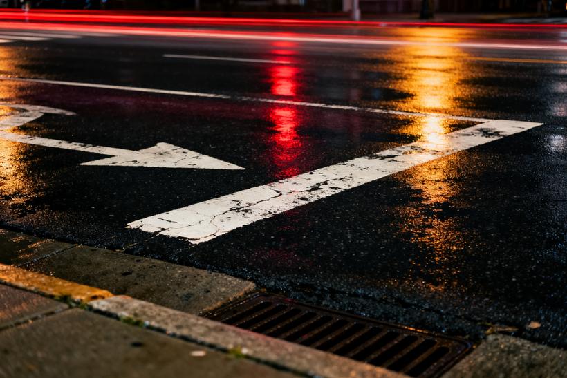 A rain-soaked intersection at night, red and amber light streaks across wet asphalt